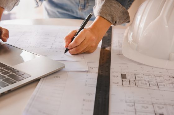 Engineers holding a pen pointing to a building and drawing outlay construction plan as guide for builders with details.Engineering and construction concept.